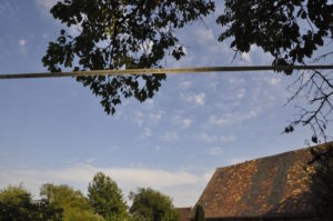 a line of paper with words printed on it, seen bisecting a landscape. The landscape is a blue sky on a summer's day, with the tops of trees and the red roof of an old farm building also visible.