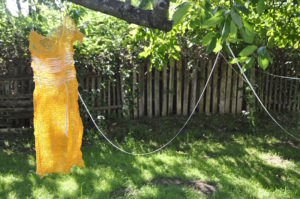 a dress made of sack-cloth, hanging outside on a tree. A trail of words on paper is sewn through the dress,
